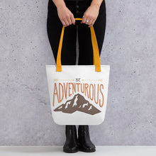 Load image into Gallery viewer, A woman holding a tote bag with yellow handles and the tote bag is a white/off white color. The design of the quote “Be Adventurous” with arrows pointing to the word “be” and a mountain illustration underneath the word “adventure.”
