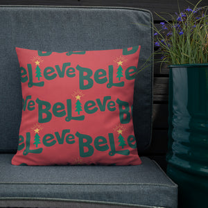 The white pillow is leaning on a sofa with a plant off to the side. The red pillow features the word Believe in green with the "I" as an illustrated Christmas tree. The word repeats in a pattern on the pillow. 