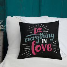 Load image into Gallery viewer, A square black pillow sits on a white sofa. The pillow reads &quot;Do everything in love&quot; in bright pink and blue hand-lettering style, with white dashes around the words.