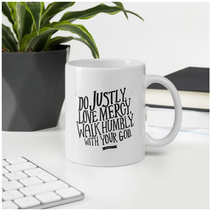 A white mug on a table with a keyboard. The mug features black lettering with the words Do justly, love mercy, walk humbly, with your God, Micah 6:8.