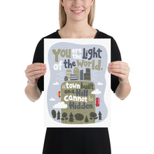 Load image into Gallery viewer, A woman holding a white piece of paper with artwork on it. The artwork is on a white background with lettering reading &quot;You are the light of the world, a town built on a hill cannot be hidden.&quot; The words are a light gray background with an illustrated city.