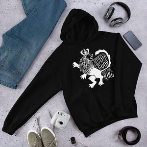 A black hoodie laying on the ground with objects around it. The hoodie features hand drawn illustration of the Chronicles of Narnia lion character Aslan. Inside the illustration there is the quote "Course He Isn't Safe, But He's Good. He's the King."