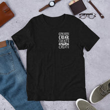 Load image into Gallery viewer, A heather black T-shirt laying flat with objects around it. The tee features the lettering and illustration in white. The phrase &quot;create, create, create, create, create&quot; is in a small rectangle on the upper left side. 