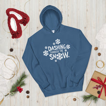 Load image into Gallery viewer, A hoodie laying on the ground with Christmas decorations and red slippers around it. The blue hoodie features the words Dashing through the snow in the middle in white. There are snowflake illustrations surrounding the words also in white. 