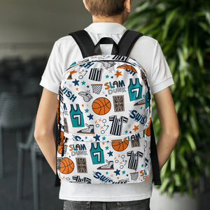 A boy with his back to the camera and dining chairs and a plant in the distance. The boy is wearing a white short sleeved polo shirt with a backpack on his shoulders. The backpack has a white background with a basketball themed pattern backpack featuring illustrated basketballs, basketball jerseys, whistles, referee shirts, basketball hoops, stars, basketball shoes, fun play sketches and the word "swish." The backpack straps are black. 