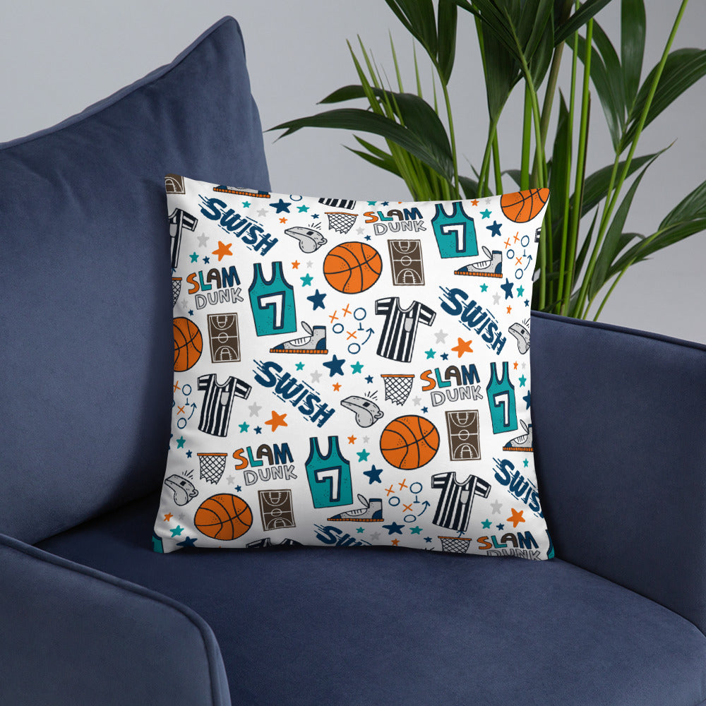 A white pillow featuring colorful basketball illustrations sits on a dark navy sofa chair with a plant in the background.