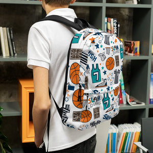 A boy standing in front of a bookshelf with his back to the camera. The boy is wearing a white short sleeved polo shirt with a backpack on his shoulders. The backpack has a white background with a basketball themed pattern backpack featuring illustrated basketballs, basketball jerseys, whistles, referee shirts, basketball hoops, stars, basketball shoes, fun play sketches and the word "swish." The backpack straps are black. 
