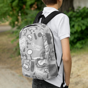 A boy faced with back to the camera and a backpack on his shoulders. The backpack is a light gray with a pattern of illustrations in darker gray and white. The pattern of illustrations features test tubes, microscopes, magnifying glasses, protective science goggles, atom models and the words "Science is cool."