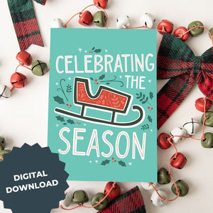 A Christmas card featured on top of some red and white Christmas decorations. The Christmas card has a light teal background with a red illustrated sleigh with holly leaves and berries around the sleigh. The words 'celebrating the season' are around the sleigh illustrated in white with a touch of red on the inside of the letters. The words "digital download" are on top of the image.
