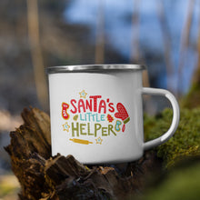 Load image into Gallery viewer, White enamel mug sitting on top of a tree branch with moss in the background. The design on the mug is in red, light blue and green. The design reads &quot;Santa&#39;s Little Helper&quot; with baking illustrations around the words. 
