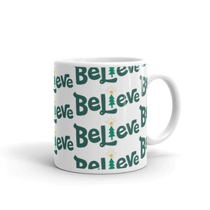 A white ceramic mug featured on a white background. The mug has a repeat pattern of the word Believe in green. The "I" of Believe is an illustrated Christmas tree. 