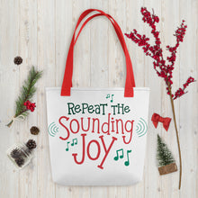 Load image into Gallery viewer, A white tote bag with red handles laying on a table with Christmas items around it. The tote bag features the words &quot;Repeat the Sounding Joy&quot; in red and green with musical notes around the words. 