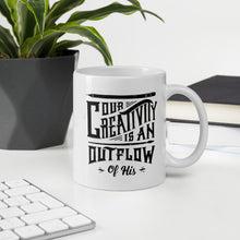 Load image into Gallery viewer, A mug featured on a desk with a plant and a keyboard. The white mug features hand drawn lettering with the words &quot;Our creativity is an outflow of His.&quot; The words are in black.
