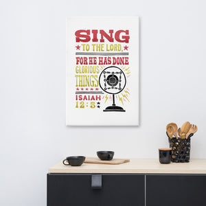 A canvas shown on a wall of a kitchen. The canvas has a white background with the words "Sing to the Lord for he has done glorious things. Isaiah 12:5." The words are in red, yellow and black. 