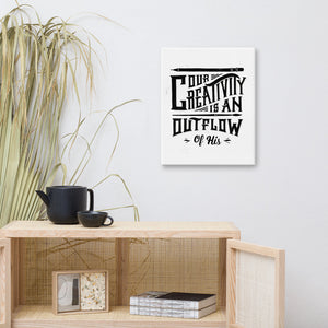 A canvas shown on a wall above a shelf. The canvas has a white background with the words "Our creativity is an outflow of His." The lettering is in black. 