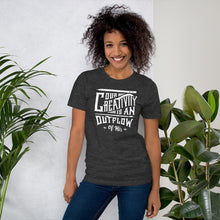 Load image into Gallery viewer, A woman wearing a dark grey short sleeved t-shirt. The tee features hand drawn lettering featuring the words &quot;Our creativity is an outflow of His&quot; in white letters.  