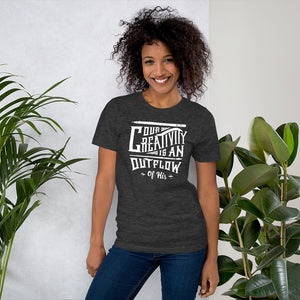 A woman wearing a dark grey short sleeved t-shirt. The tee features hand drawn lettering featuring the words "Our creativity is an outflow of His" in white letters.  