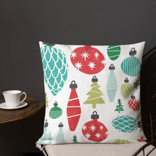 Load image into Gallery viewer, A pillow on a chair with a coffee mug on a table next to it. The white pillow features large illustrated ornaments. The ornaments are in red, green, light green and light blue. 