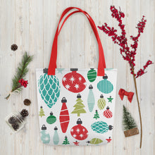 Load image into Gallery viewer, A white tote bag with red handles laying on a table with Christmas items around it. The tote bag features illustrated vintage Christmas ornaments in the colors blue, green and red in various shades. 