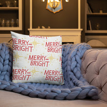 Load image into Gallery viewer, A white pillow on a sofa with a blue knitted blanket. The white pillow features a pattern of the words Merry and Bright with a pattern of Christmas stars. The words in the pattern are red and the stars are yellow. 