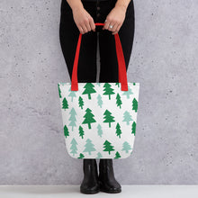 Load image into Gallery viewer, Someone holding a tote bag with red handles and a white fabric bag. The artwork features illustrated Christmas pine trees in light and dark green. 