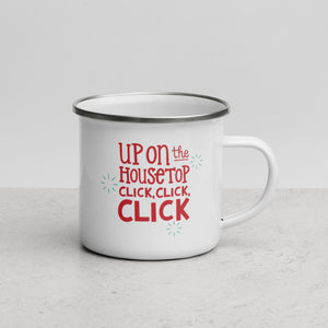 White enamel mug featured on a white table top and white background. The design is in red with the words "Up on the housetop click, click, click" with small blue stars around the words.  