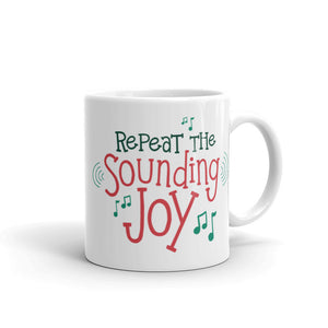 A white ceramic mug featured on a white background. The design is in red and green with musical notes around the words. The words read "Repeat the Sounding Joy."