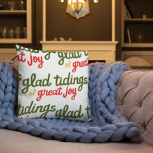 Load image into Gallery viewer, A white pillow on a sofa with a blue knitted blanket. The white pillow features the words &quot;glad tidings of great joy&quot; in a repeat pattern in the colors red, green and yellow. 