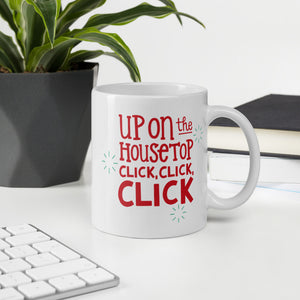A mug featured on a desk with a plant and a keyboard. The illustrated design says "Up on the housetop, click, click, click" in red with small blue stars around it. 