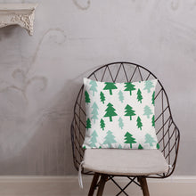 Load image into Gallery viewer, The pillow is leaning on a metal chair with a cushion. The white pillow features dark and light green pine tree illustration.