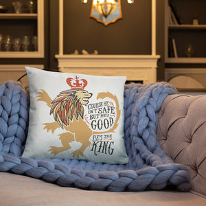 A white pillow on a crochet blue blanket on a sofa. The artwork features hand drawn illustration of the Chronicles of Narnia lion character Aslan. Inside the illustration there is the quote "Course He Isn't Safe, But He's Good. He's the King."