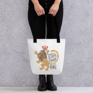 A woman holding a white tote bag with black handles. The artwork features an illustrated with the words "Course He Isn't Safe, But He's Good. He's the King."