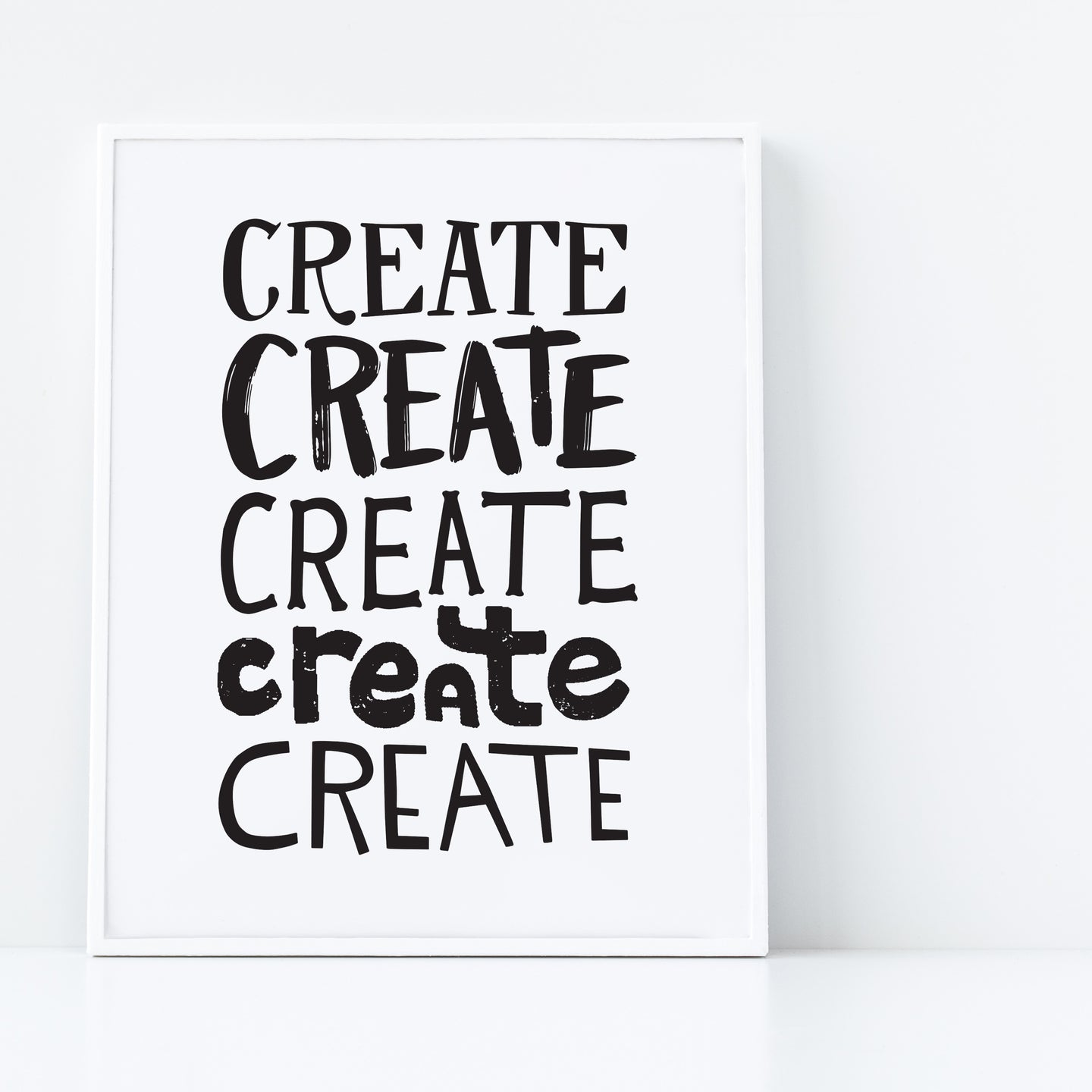 A print featured in a white frame with the word “create” five times in black lettering. 