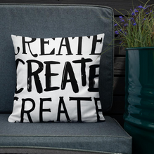 Load image into Gallery viewer, A pillow leaning on a grey sofa with a plant in the background. The white pillow features the phrase “create create create” in black letters.