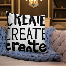 Load image into Gallery viewer, A pillow on a sofa with a blue knitted blanket with the phrase “create, create, create&quot; in black lettering with each word in three different fonts. 