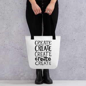 Someone holding a tote bag with black handles and a white fabric bag. The lettering is in black and features the words "create, create, create, create, create" with each word in a different hand lettered font.