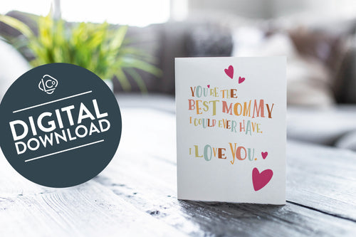 A greeting card featured on a black, wood coffee table. There’s a white planter in the background with a green plant. There’s also a gray sofa in the background with a white pillow. The card features the words “You’re the best mommy I could ever have. I love you.” The words 