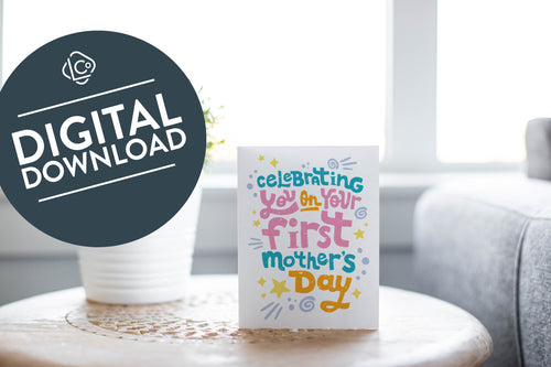 A photo of a card featured on a tabletop next to a white planter filled with a green plant. ​​The card features the words “Celebrating you on your first Mother’s Day.” The words 