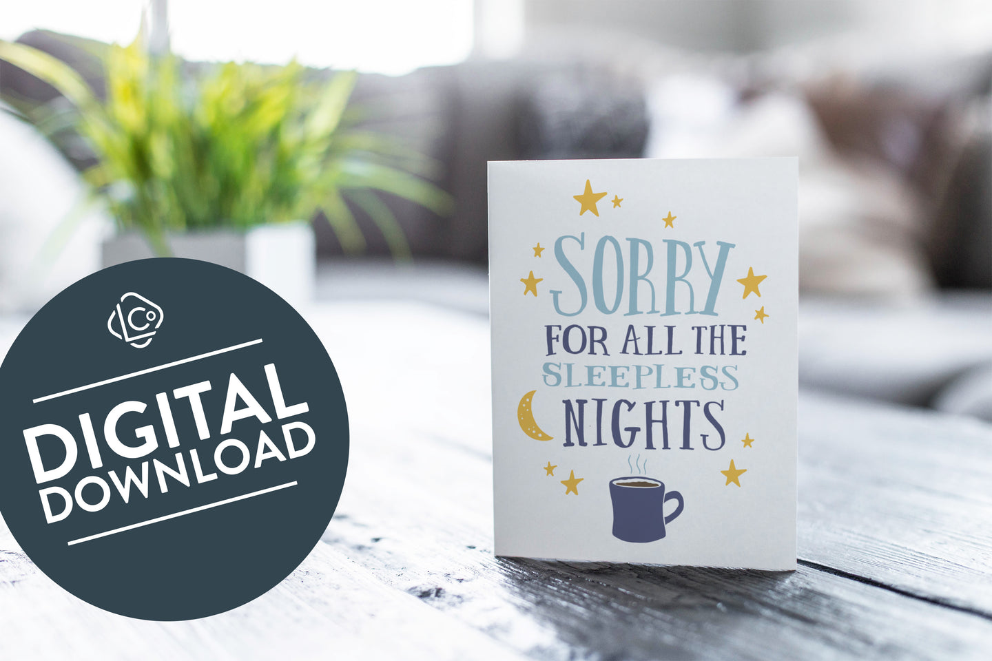 A greeting card featured on a black, wood coffee table. There’s a white planter in the background with a green plant. There’s also a gray sofa in the background with a white pillow. The card features the words “Sorry for all the sleepless nights.” The words 