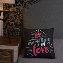 Load image into Gallery viewer, A square black pillow sits on a grey bedspread in front of a wallpapered wall. The pillow reads &quot;Do everything in love&quot; in bright pink and blue hand-lettering style, with white dashes around the words.