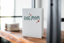 Load image into Gallery viewer, A card on a wood tabletop with an object in the background that is out of focus. The card features the words “Dog mom.”