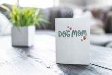 Load image into Gallery viewer, A greeting card featured on a black, wood coffee table. There’s a white planter in the background with a green plant. There’s also a gray sofa in the background with a white pillow. The card features the words “Dog mom.” 