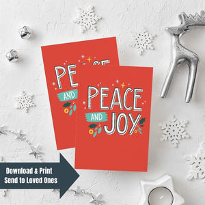 Two Christmas cards laying on a white background with white and silver Christmas decorations on the table. The card has a red background with the words "peace and joy" in white and illustrations of stars and holly leaves around the wording. The words "download & print, send to loved ones" are on top of the image in the bottom lefthand corner.