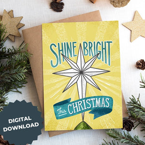 A photo of a Christmas card on top of a brown paper wrapped gift with Christmas decor around it. The Christmas card has a yellow background with the words 'shine bright this Christmas' in blue and white. There's an illustrated vintage star Christmas tree topper featured in between the words. The words "digital download" are in the lefthand corner over the image.