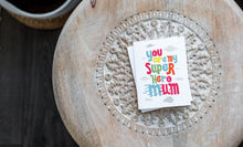 Load image into Gallery viewer, A greeting card laying on a wooden table with some cut wood details. The card features the words “You are my super hero mum” with clouds in the background. 