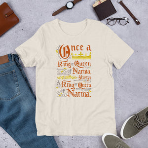 A dust color short sleeved T-shirt laying flat with objects around it. The T-Shirt features hand lettering with the CS Lewis quote "Once a king or queen of Narnia, always a king or queen of Narnia."