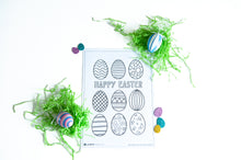 Load image into Gallery viewer, A coloring sheet on a white tabletop. There’s fake Easter grass around the color page. The coloring page features illustrated Easter eggs with fun patterns to color in with the words “Happy Easter” in the middle of the eggs. 