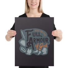 Load image into Gallery viewer, A smiling woman holds up a dark gray canvas. The canvas features the quote &#39;Put on the full armour of God&#39; in black and orange typography, with medieval-style pieces of armour illustrated in pale gray.
