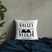 Load image into Gallery viewer, A monochrome square pillow sits on a blue bedspread against a grey concrete wall. The pillow design is black on a white background, and reads &#39;Every valley shall be lifted high&#39; in a variety of typographic lettering, with flourishes and an illustration of two mountain peaks. 