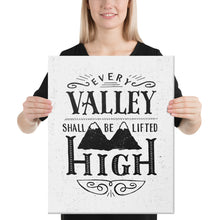 Load image into Gallery viewer, A smiling woman holds up a monochrome black and white print. The print reads &#39;Every valley shall be lifted high&#39; in a variety of typographic lettering, with flourishes and an image of two mountain peaks. 